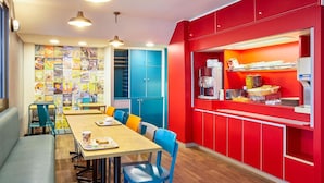 Un espace repas comprenant une longue table, des chaises et un coin café avec une machine à café et des en-cas.