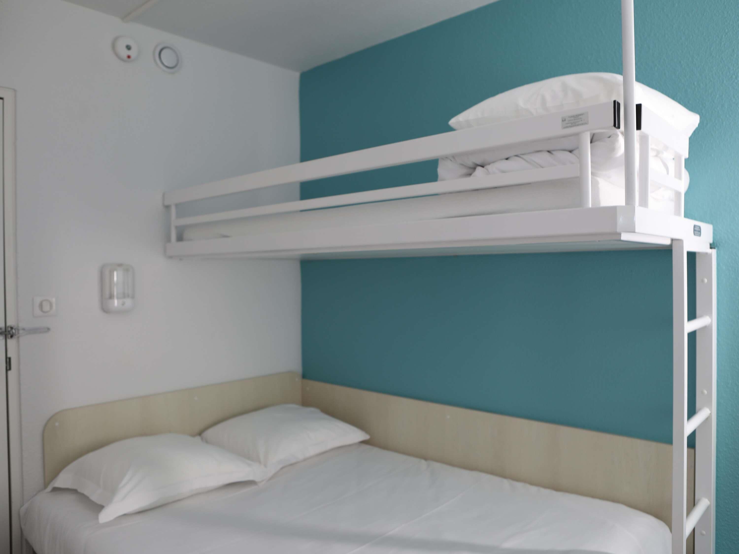 Un lit superposé avec un matelas et des oreillers blancs, une porte blanche et un mur de couleur turquoise.