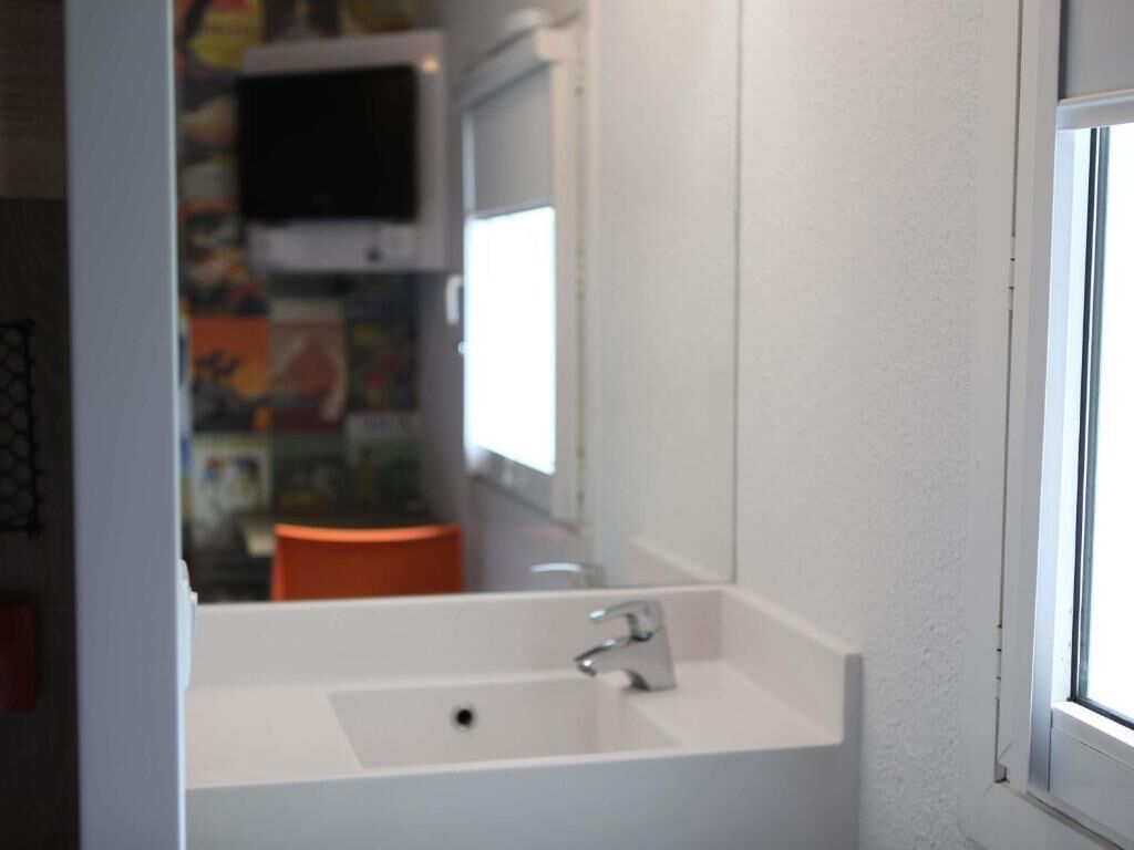 Une salle de bain avec un lavabo blanc, un miroir et une fenêtre.