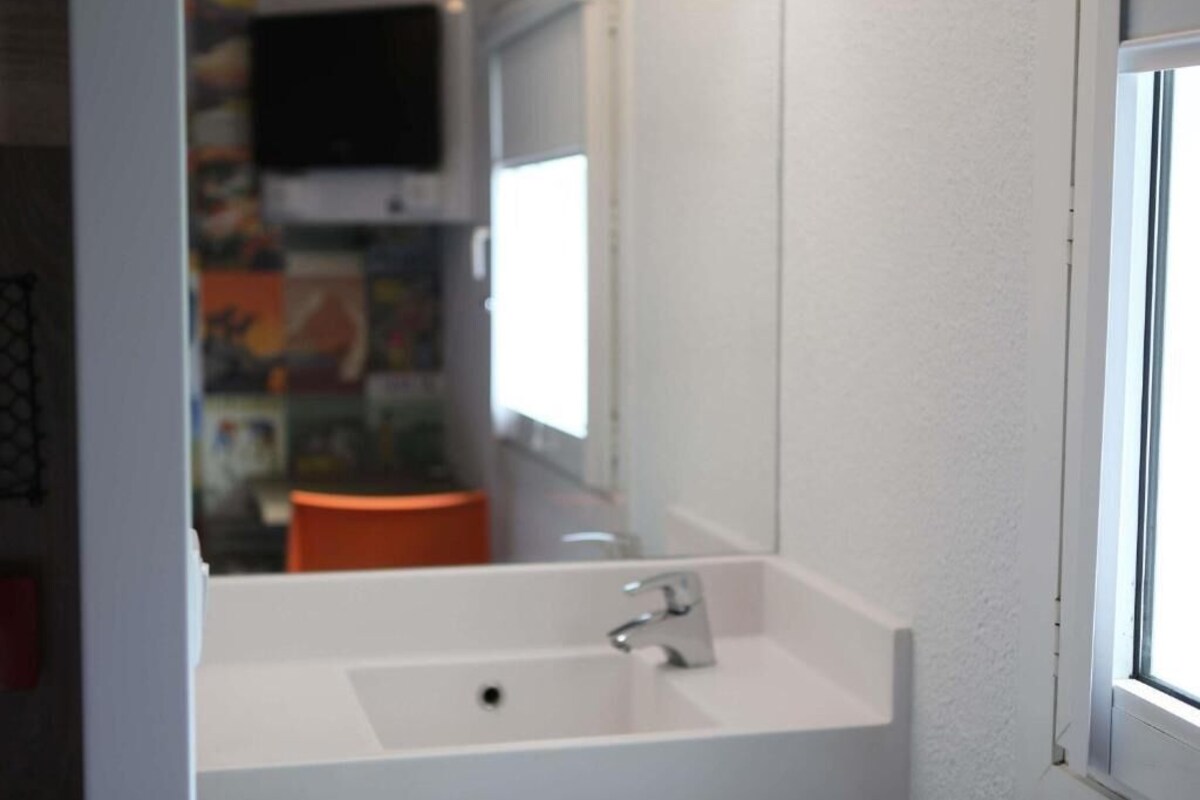 Een badkamer met een wit wastafel, een spiegel en een raam.