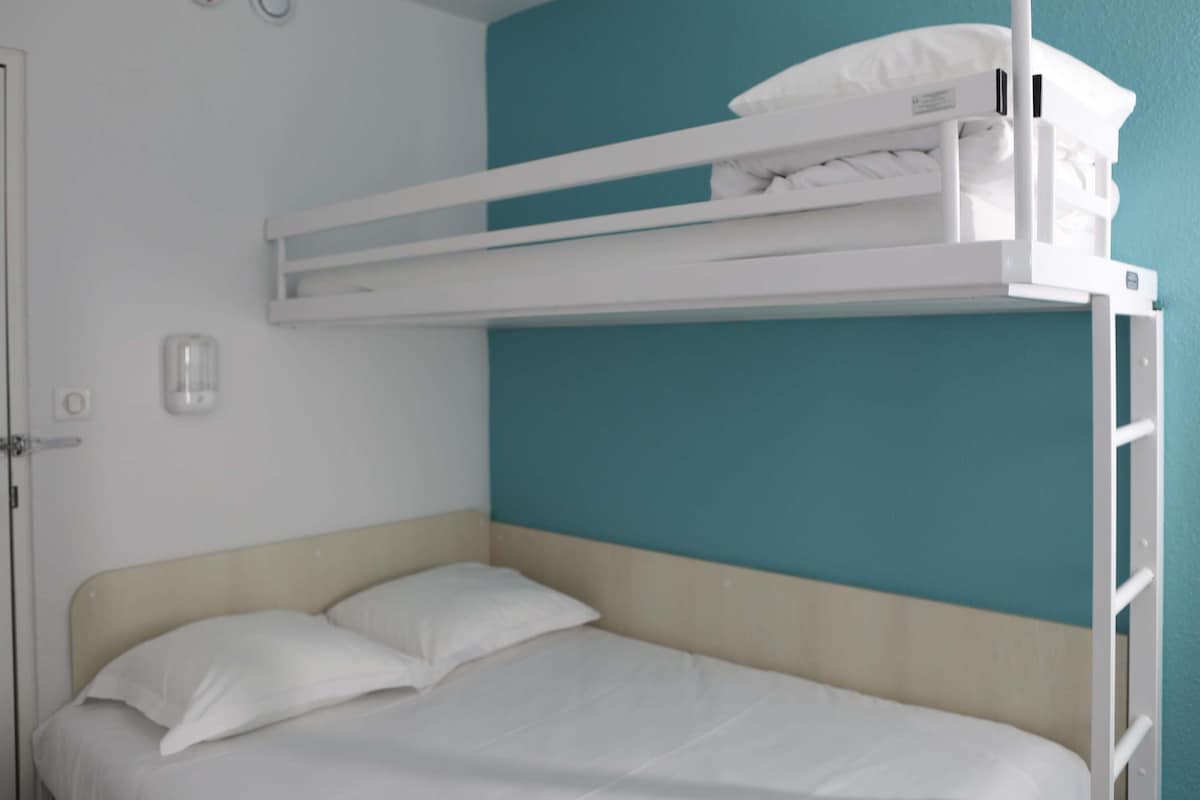 Una cama litera con colchón y almohadas blancos, una puerta blanca y una pared color verde azulado.