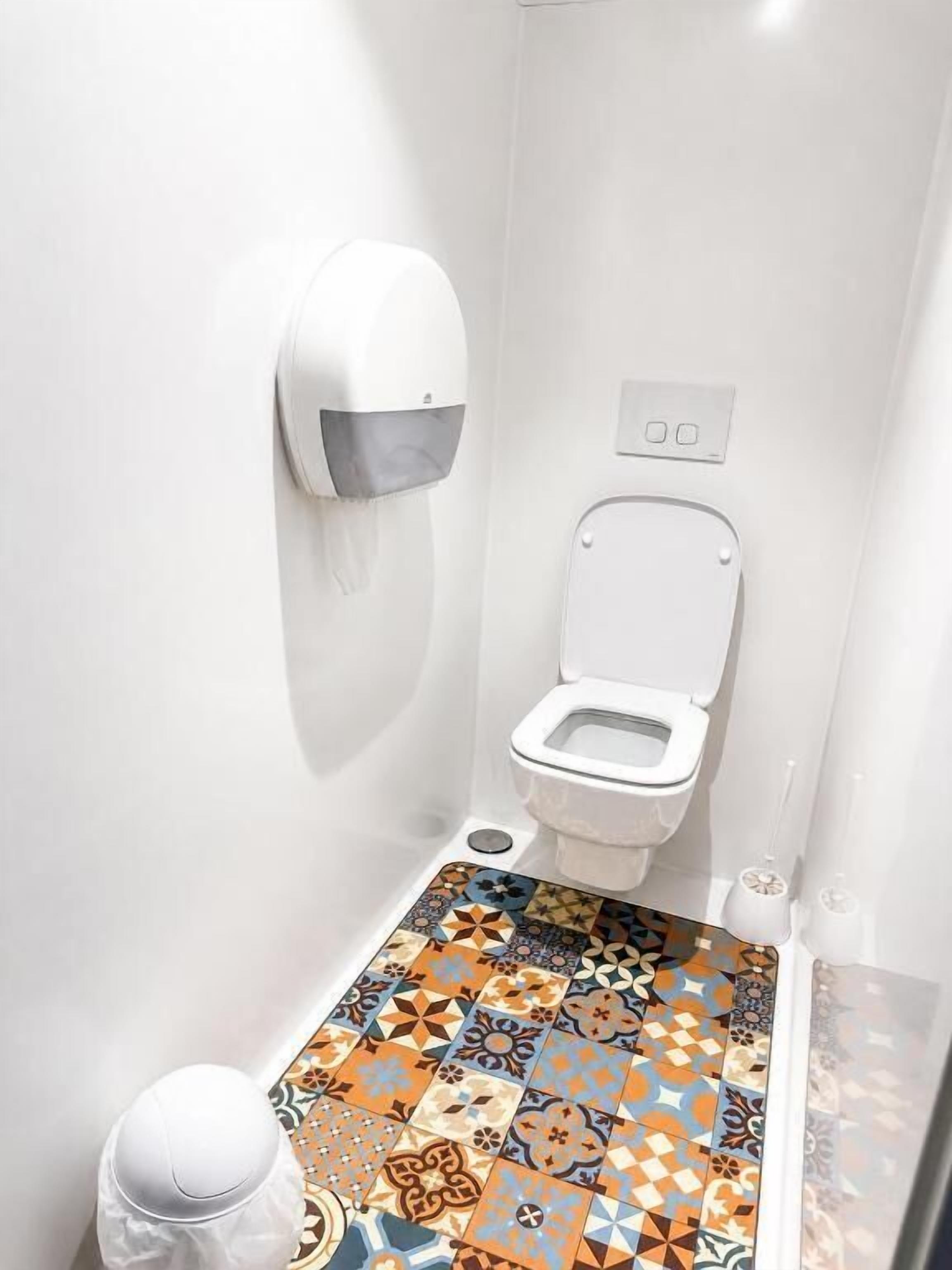 A small bathroom with a toilet, a hand dryer, and a patterned floor.