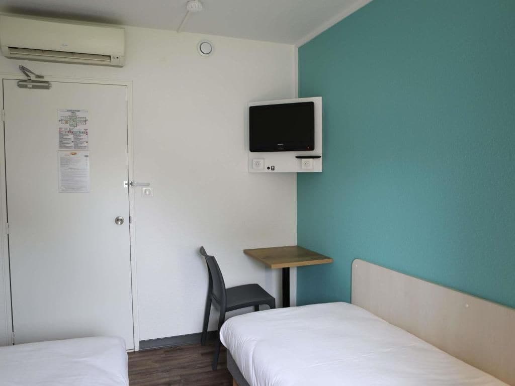 Habitación de hotel con dos camas, un escritorio, una silla, un televisor y un equipo de aire acondicionado.