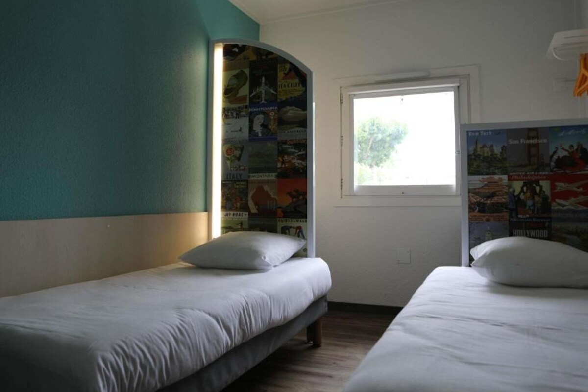 Een kamer met twee eenpersoonsbedden, een raam met uitzicht en een wand versierd met reisposters.