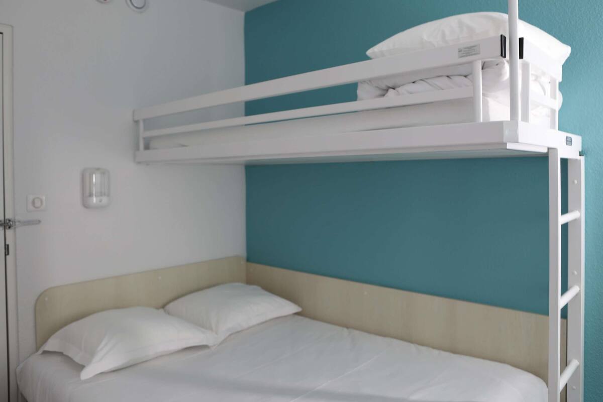Ein Stockbett mit weißer Matratze und Kissen, eine weiße Tür und eine türkisblaue Wand.