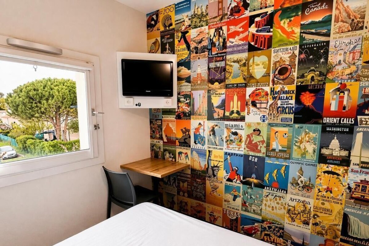 Een hotelkamer met een bed, een aan de muur bevestigde televisie, een bureau en een muur versierd met reisposters.