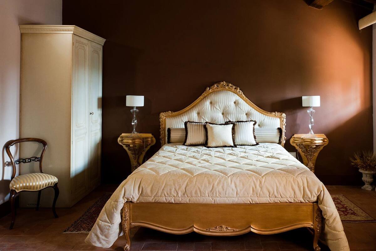 A large bed with a tufted headboard, two bedside tables with lamps, a chair, and a cabinet.