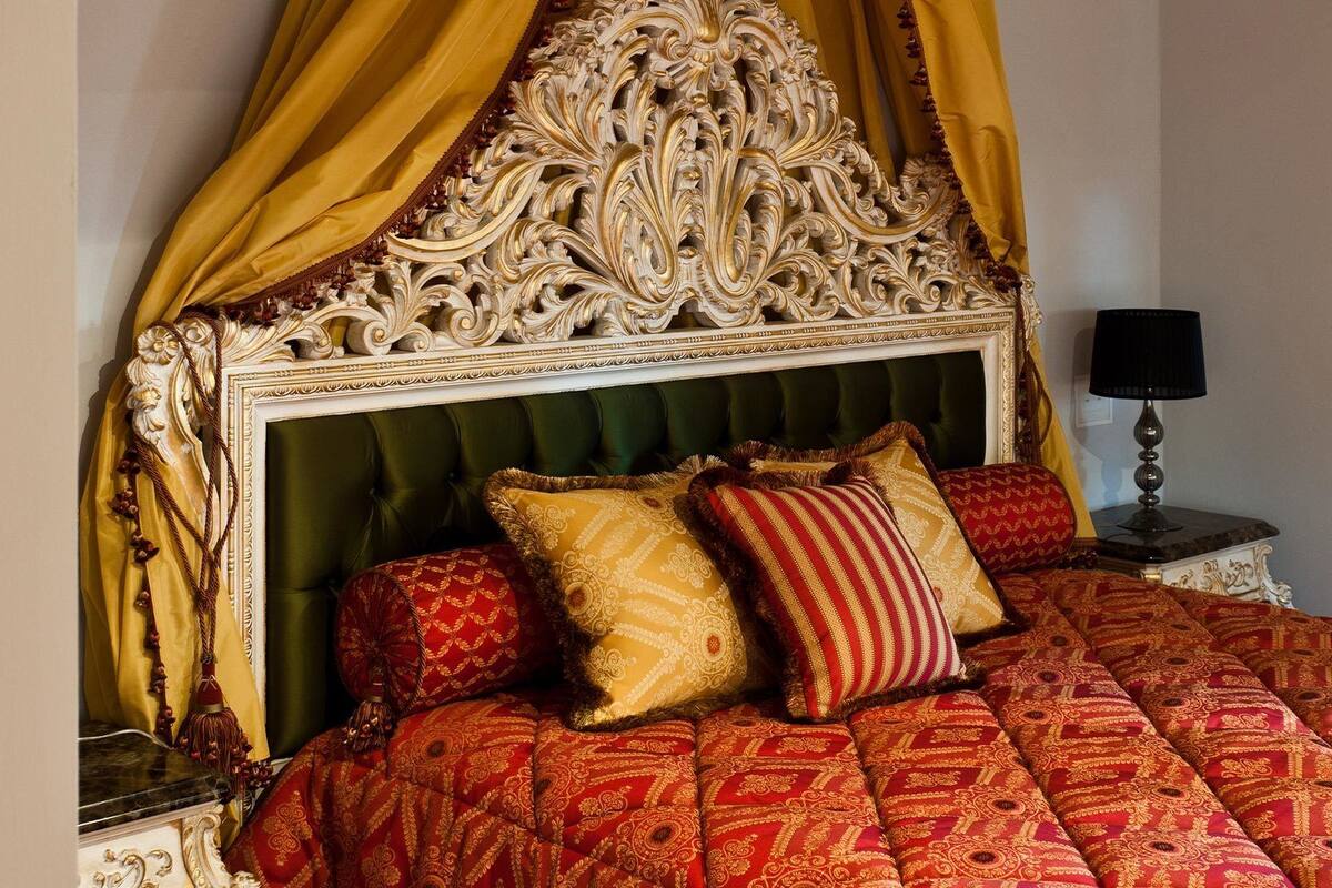 A bed with a green upholstered headboard, a yellow draped canopy, and multiple patterned pillows.