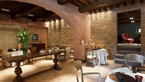 A dining area with a long wooden table, chairs, and a stone wall. - Villa Armena (Buonconvento)