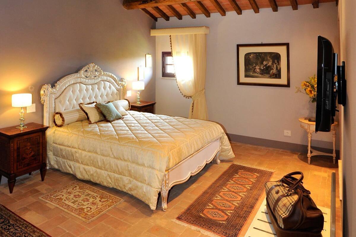 A bedroom with a large bed, two bedside tables, a nightstand, a television, and a rug.