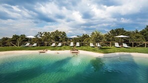 A pool area with clear water, surrounded by white lounge chairs and umbrellas, under a cloudy sky. - Villa Armena (Buonconvento)