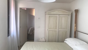Ein Schlafzimmer mit Bett, Kleiderschrank, einer Tür zu einem anderen Raum und einer Hängeleuchte.