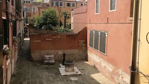 Ein schmaler Gang mit Häusern an beiden Seiten, ein kleiner Garten mit einem Baum und ein traditioneller Brunnen.