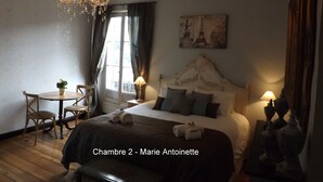 A bedroom with a bed, a chandelier, a table with chairs, and a painting on the wall. - Maison Porte Del Marty (Lalinde)