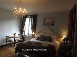 Quarto com cama, lustre, mesa com cadeiras e um quadro na parede.