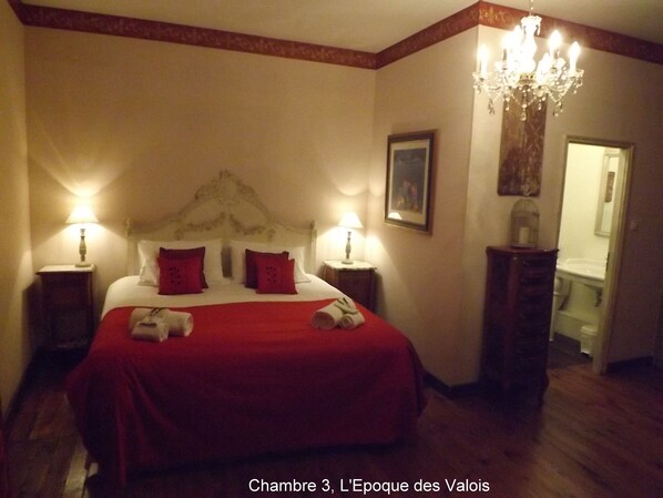 A hotel room with a large bed, two bedside lamps, a chandelier, and a painting on the wall. - Maison Porte Del Marty (Lalinde)