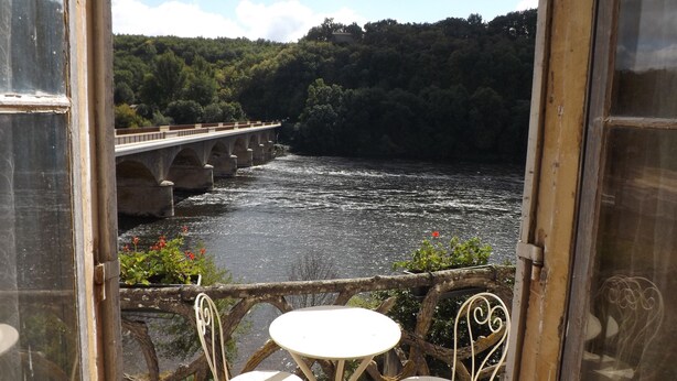 A view from a balcony with a table and chairs, overlooking a river and a bridge. - Maison Porte Del Marty (Lalinde)