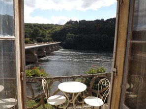 A view from a balcony with a table and chairs, overlooking a river and a bridge. - Maison Porte Del Marty (Lalinde)
