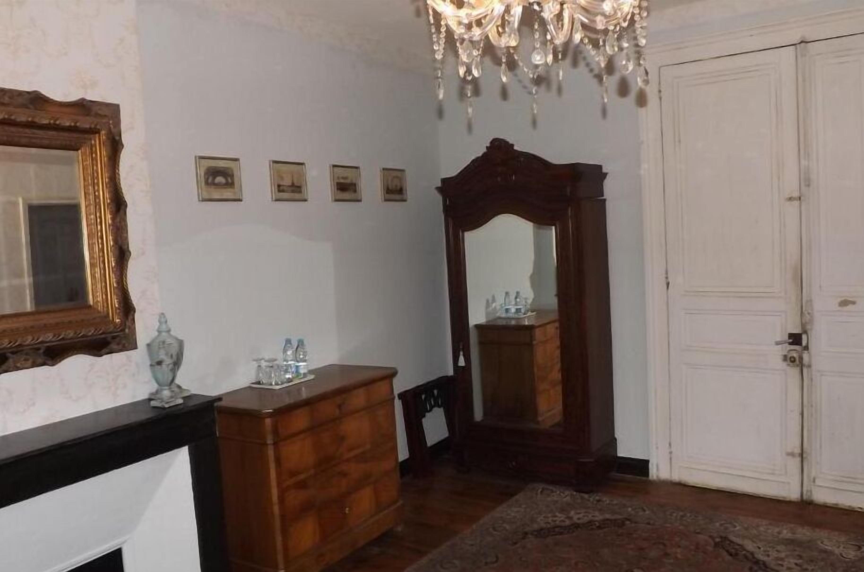A room with a wooden dresser, a large mirror, a chandelier, and a white door.
