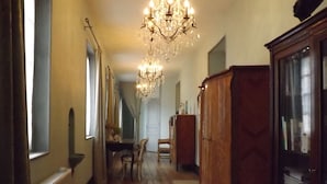 A hallway with wooden flooring, a chandelier, a dining table with chairs, and a cabinet with glass doors. - Maison Porte Del Marty (Lalinde)