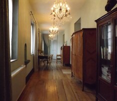 Um corredor com piso de madeira, um candelabro, uma mesa de jantar com cadeiras e um armário com portas de vidro.