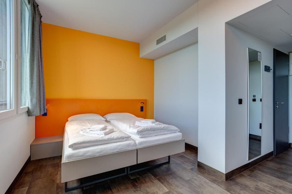 A modern hotel room with a bed, a small bedside table, and a wardrobe.