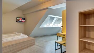 Ein modernes Schlafzimmer mit schrägen Wänden, einem Bett, einem Schreibtisch und einem an der Wand befestigten Fernseher.