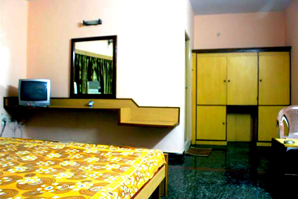 Quarto de hotel com cama, televisão, guarda-roupa e espelho.