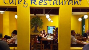 A restaurant interior with a yellow theme, tables, chairs, and patrons dining. - Vinodhara Guesthouse (Tirukalukundram)