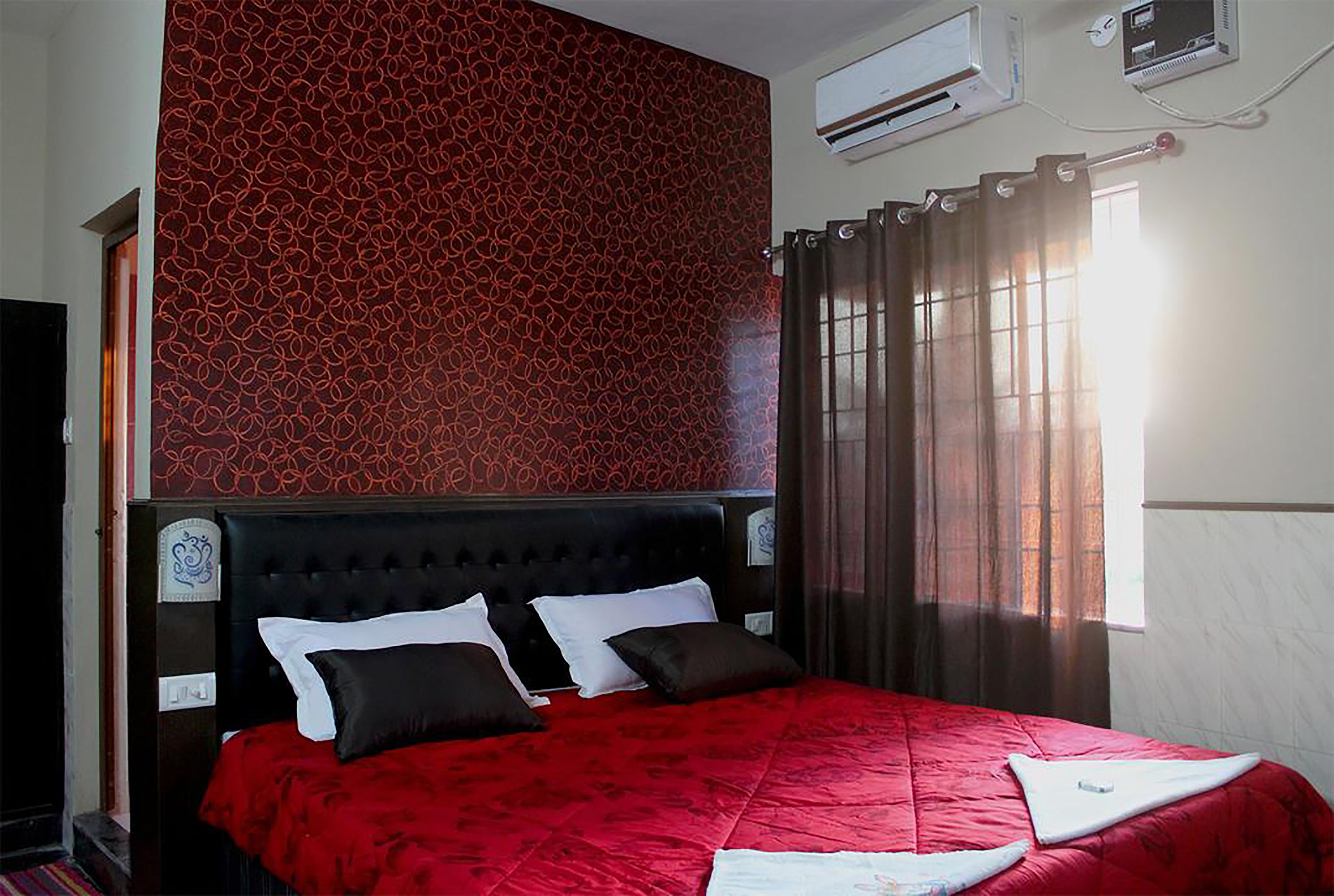 A bedroom with a red patterned wall, a black upholstered headboard, and a red bedspread.
