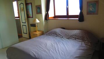 Quarto com cama, mesa de cabeceira com luminária, janela com cortinas e porta.