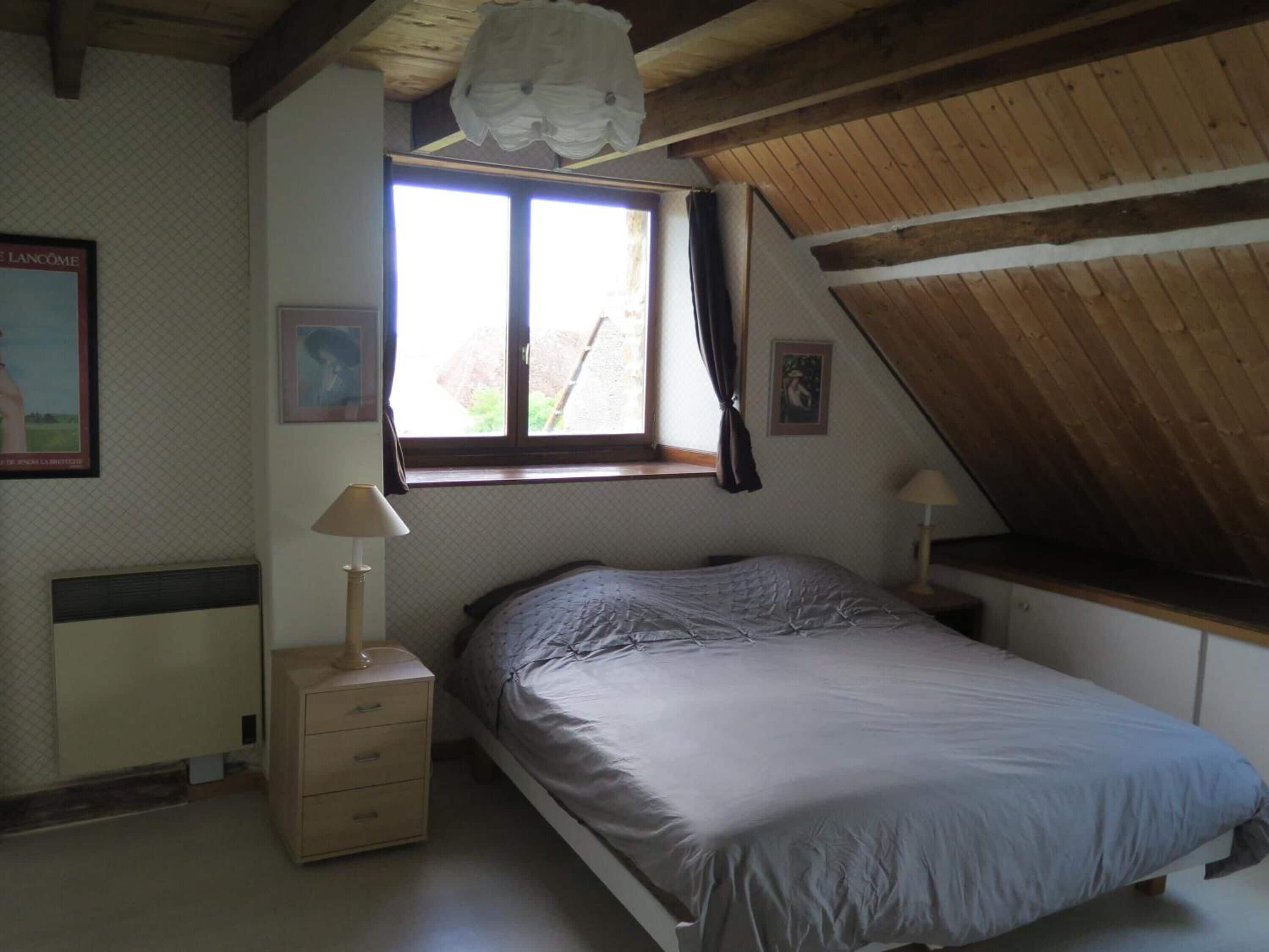 Un dormitorio con una cama individual, una ventana con cortinas, una lámpara de noche y un radiador.