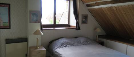 A bedroom with a single bed, a window with curtains, a bedside lamp, and a radiator.