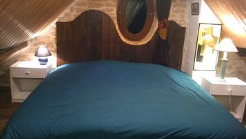 A bedroom with a large bed, wooden headboard, and a circular mirror. There are bedside tables with lamps and a small shelf.