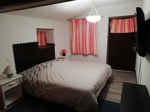 A bedroom with a bed, a bedside table, a lamp, a mirror, a TV, and a window with curtains. - Chambres d'hôtes au verger de Marcilly (Marcilly-Ogny)