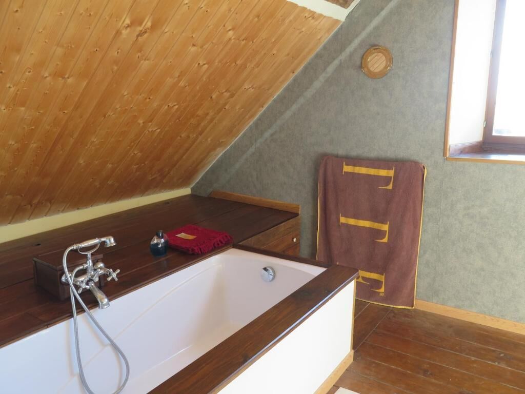Un baño con techo inclinado de madera, una bañera blanca, un cabezal de ducha y una toalla colgada en la pared.