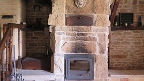 Una chimenea de piedra con una puerta de metal, una escalera de madera y una pared de piedra con una cabeza tallada.