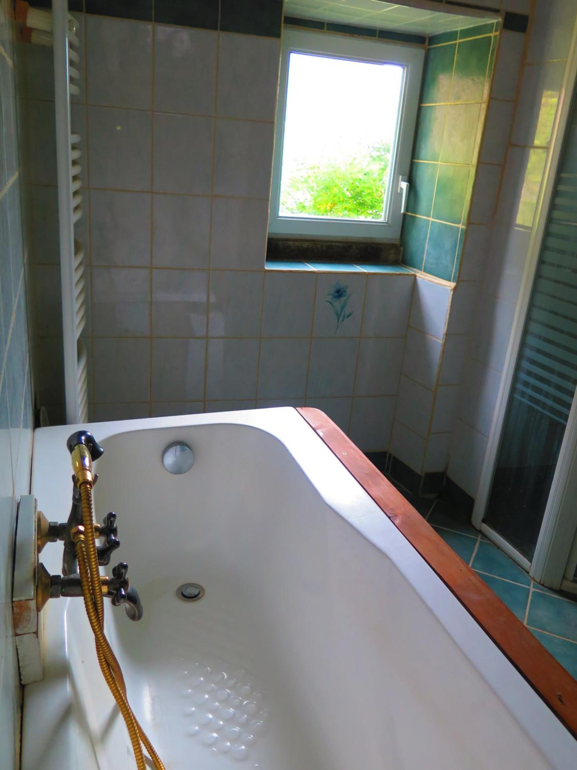 A bathroom with a bathtub, a window, and tiled walls.