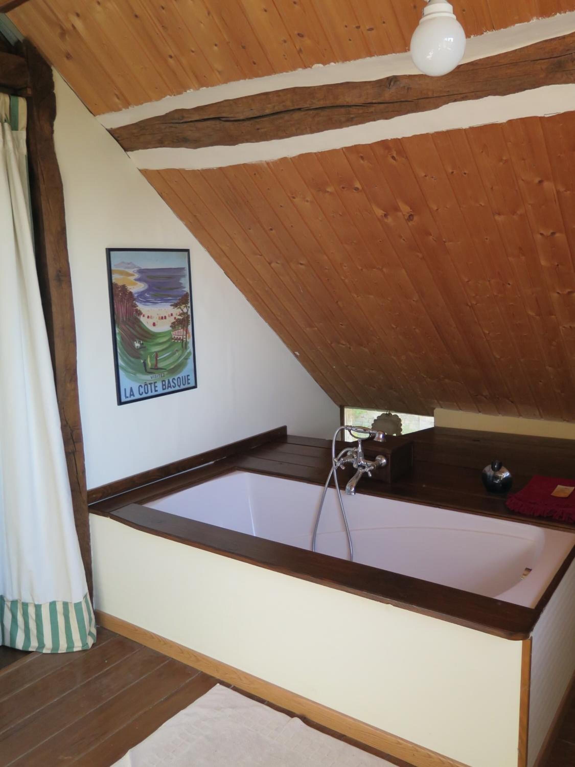 Een kamer met een houten plafond, een wit ligbad, een lijst met een foto aan de muur en een klein tafeltje met een waterkoker.