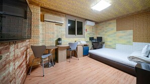 A compact room with a bed, a desk, two chairs, and a small kitchenette area.