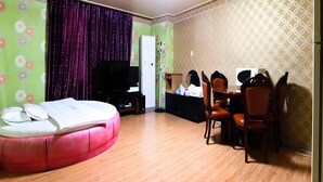 A room with a dining area, a television, and a bed with a pink headboard.