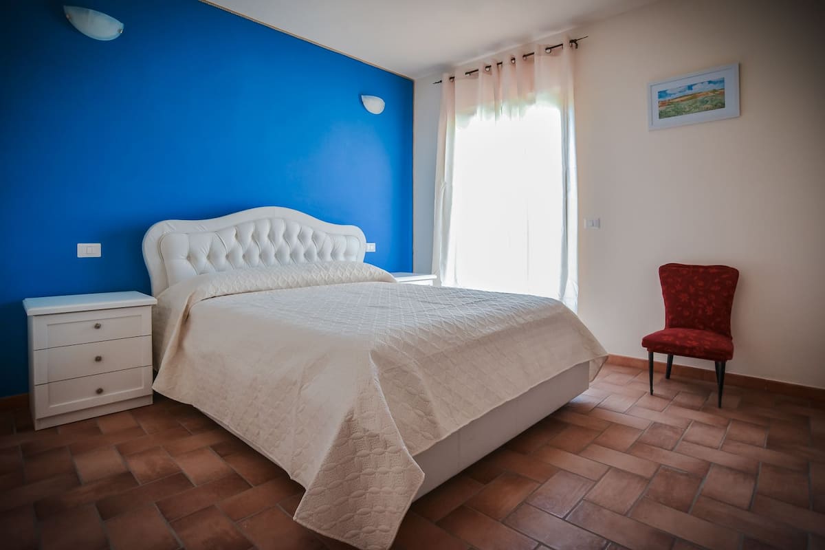 A bedroom with a bed, a nightstand, a chair, and a painting on the wall.