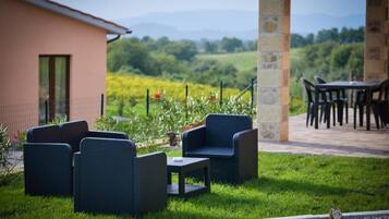 Un patio con mobiliario de mimbre, un pilar de piedra y vistas a un viñedo.