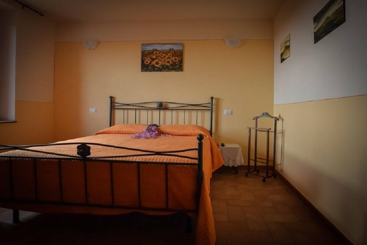 A bedroom with a metal bed frame, an orange bedspread, a small table with a white cloth, and a radiator.