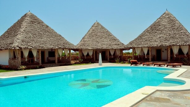 A swimming pool with three thatched-roof huts, each with a covered veranda. - Coral Sea Villas (Malindi)