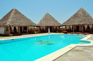Una piscina con tres cabañas de techo de paja, cada una con un porche cubierto.