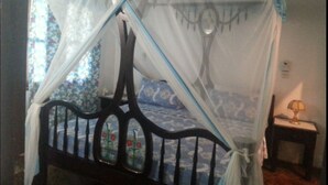 A bed with a canopy, a nightstand with a lamp, and a floral-patterned wall. - Coral Sea Villas (Malindi)