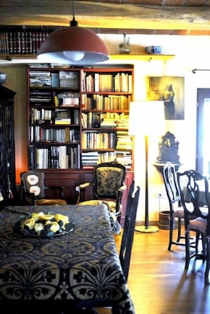 Un comedor con un mantel estampado, una estantería llena de libros y una lámpara antigua.