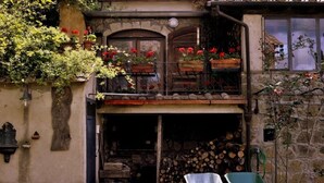 A rustic building with a stone facade, a wooden balcony with red flowers, and a pile of firewood. - Agriturismo Solidor (Pitigliano)