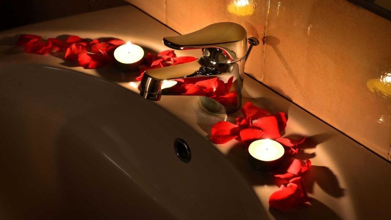 A bathroom sink with a faucet, candles, and rose petals.